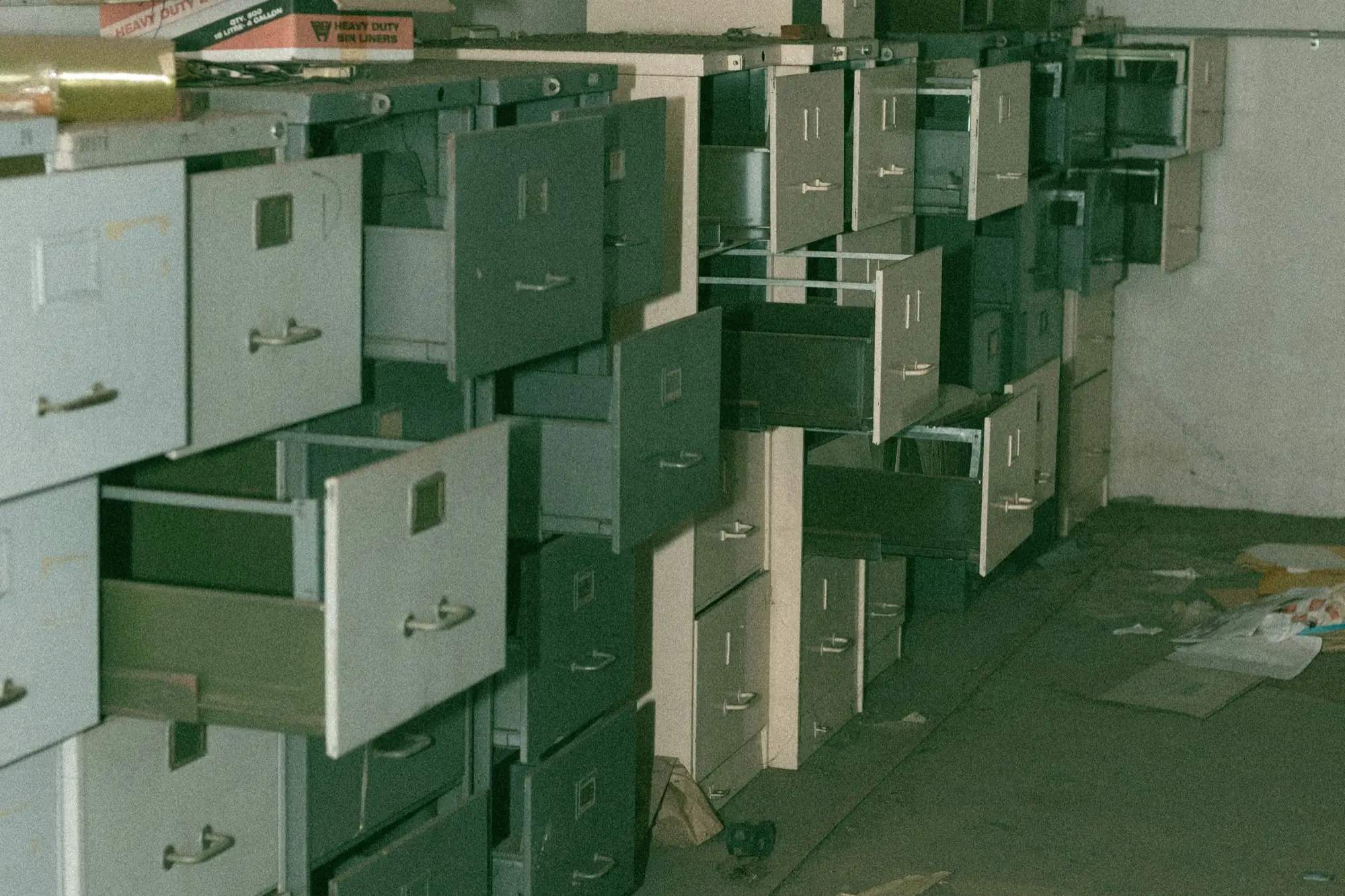 An abandoned archive of filing cabinets with every drawer pulled open — the clerks are gone, the records remain