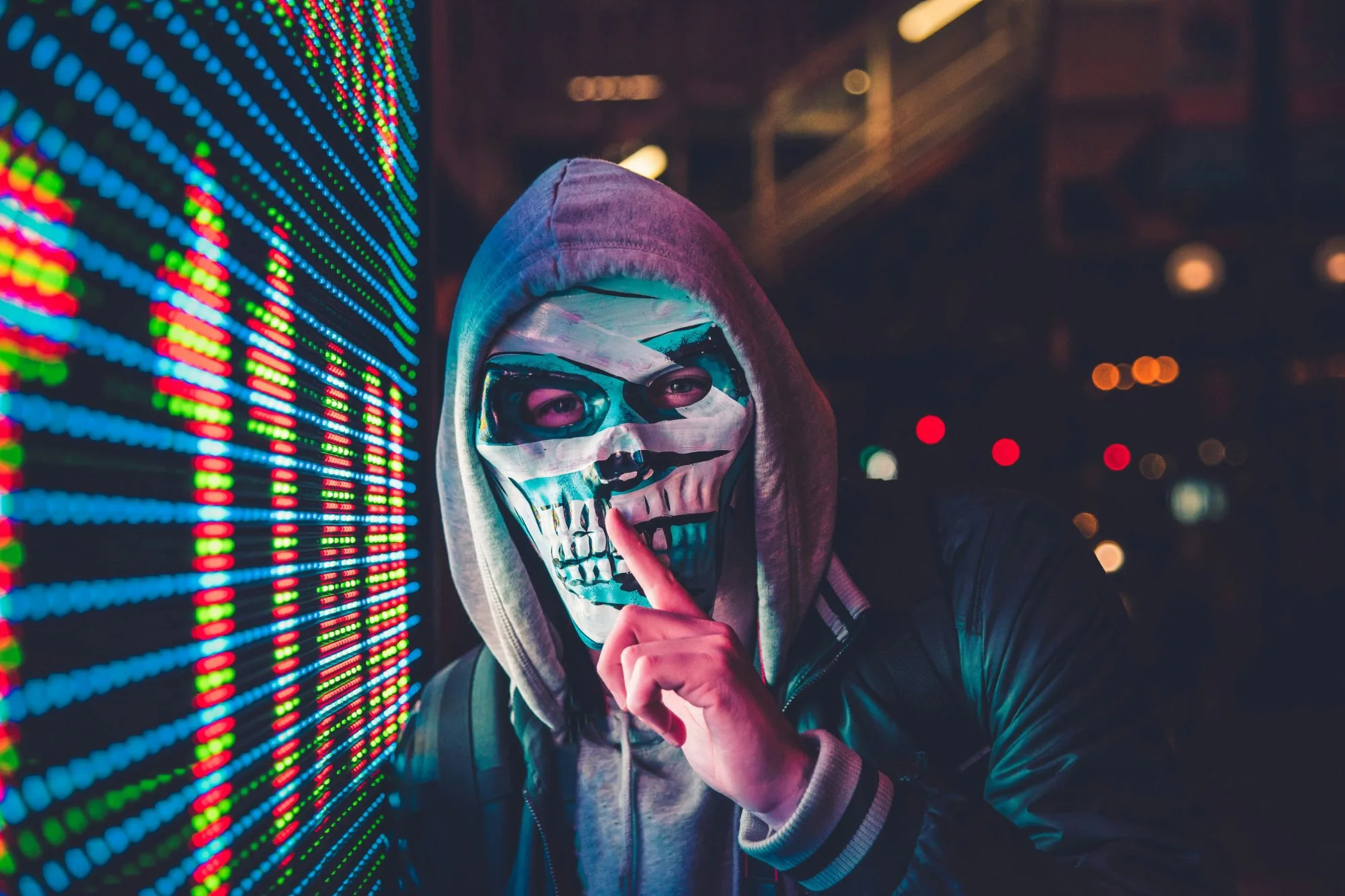 Anonieme figuur met schedelmasker naast LED-display &mdash; autonome AI-aanvallen op bedrijfsplatforms